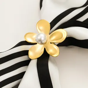Golden flower silk scarf ring with pearl center on a striped fabric background