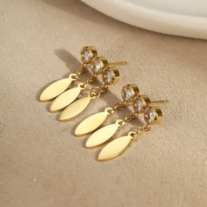 Golden stainless steel tassel earrings with zircon studs and leaf charms on beige background