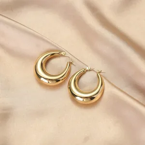 Detail van dikke gouden oorringen op champagne zijden stof met gepolijste glanzende textuur