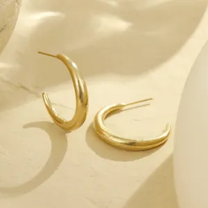 Detailweergave van dikke C-vormige oorringen met mat geborstelde 18K gouden textuur
