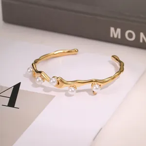Detail of a wave shaped gold stainless steel bangle with five white pearls inlay