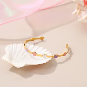 Detail eines goldenen Armreifs mit bunten Emaille-Schmetterlingen auf rosa Grund