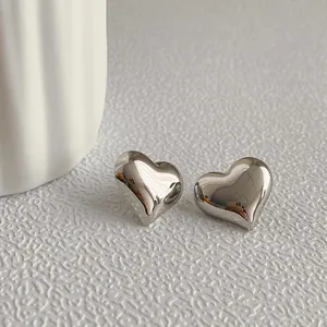 Macro detail of polished silver metal heart stud earrings on a minimalist white background