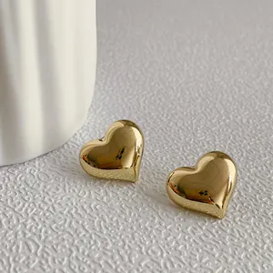 Top macro view of polished gold heart stud earrings on textured surface background