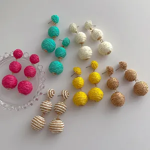 Macro detail of six pairs colorful woven raffia ball earrings in various vibrant summer hues