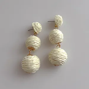 Detail of cream raffia woven triple drop earrings with gold metal accents