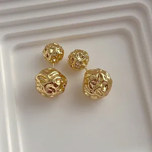 Détail de boucles d'oreilles dorées à double sphère métallique plissée sur support blanc