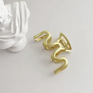 Macro shot of matte gold wave-shaped hair claw clip with spring and non-slip teeth