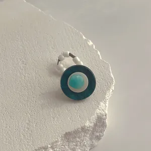 Detailansicht eines handgefertigten Muschelrings mit blauem Stein auf Steinsockel