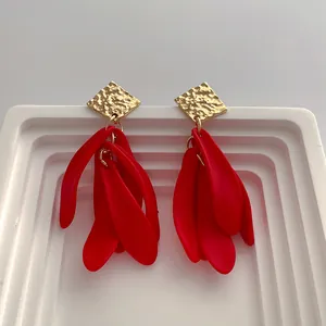 Detail of red petal earrings with gold hammered square studs on white pedestal