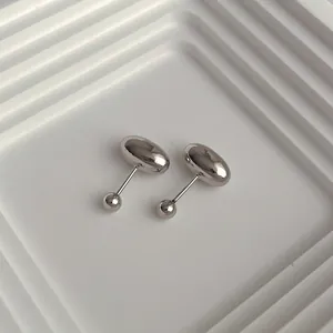 Minimalist silver bean stud earrings with screw-back closures on a textured tray