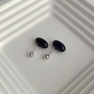 Macro view of black enamel mini oval stud earrings with secure ball screw back closure