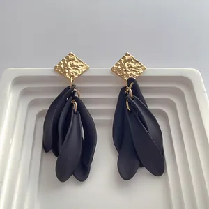 Close-up of hammered gold square stud with matte black resin petal drop earrings
