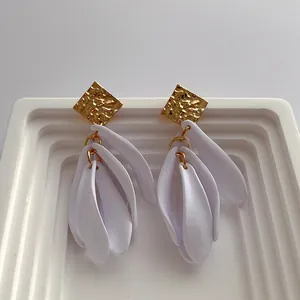 Detail of gold hammered metal stud and white matte resin petal pendant on earrings