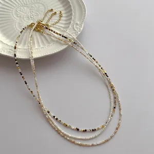 Detailed close-up of 2mm shell pearl necklace with golden lobster clasp on white ceramic plate
