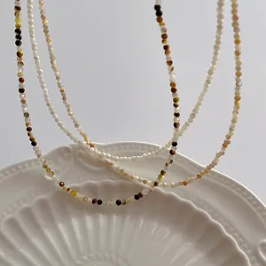 Macro view of multi-color 2mm pearl and shell bead necklaces on white ceramic plate