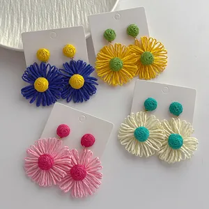Detail van handgemaakte raffia bloemoorbellen in blauw geel roze en beige kleuren