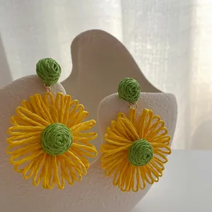 Detailweergave van handgemaakte zonnebloem oorbellen van raffia op wit keramiek plateau