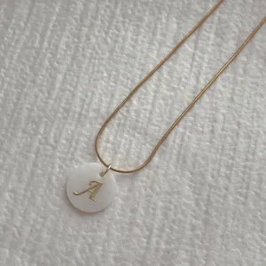 Detail of gold snake chain with a white shell pendant featuring a golden letter A