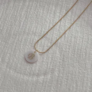 Macro detail of natural shell pendant necklace with golden letter B and snake chain