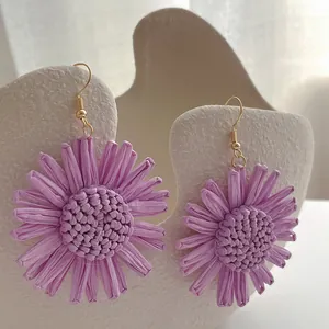 Detaillierte Makroansicht lila Raffia-Sonnenblumenohrringe mit handgewebter Textur