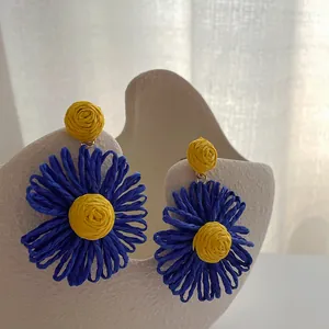 Detail van handgemaakte raffia madeliefje oorbellen in blauw en geel weefsel