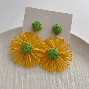 Detail van handgemaakte gevlochten raffia zonnebloem oorbellen met gele bladen en groen