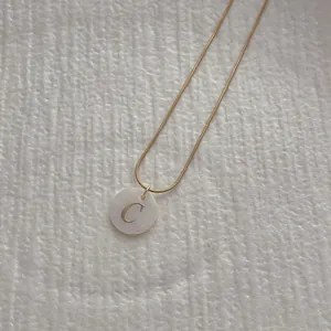Detail view of a shell alphabet necklace with golden letter C on a snake chain