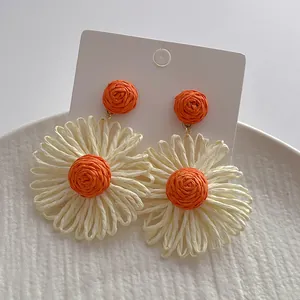 Detail van handgemaakte raffia madeliefjes oorbellen met oranje kralen en witte bloemen