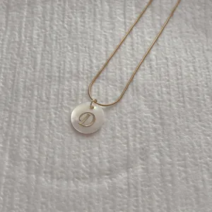 Macro shot of letter D pendant on gold snake chain with white shell inlay detail