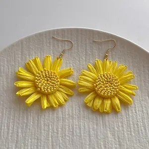 Detail von handgefertigten gelben Bast-Sonnenblumenohrringen mit goldenen Metallhaken