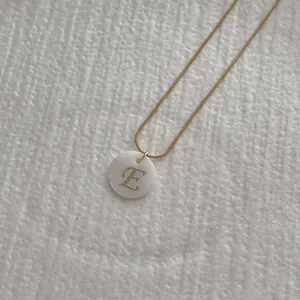 Close-up of golden snake chain necklace with a white shell letter E pendant