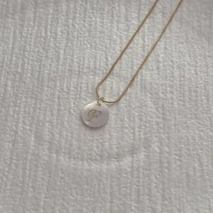 Detail of golden snake chain and letter F shell pendant necklace with soft lighting