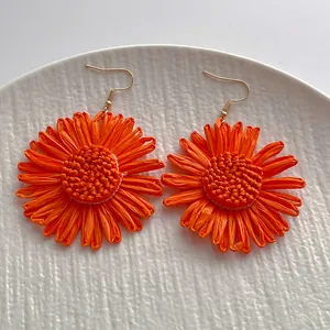 Handgefertigte orangefarbene Raffia-Blumenohrringe im Boho-Stil auf weißem Teller