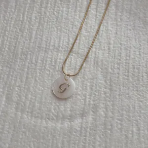 Macro shot of letter G pendant on snake chain with natural white shell inlay detail