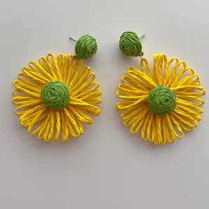 Detailopname van handgemaakte gele raffia zonnebloem oorbellen met een groen middenstuk
