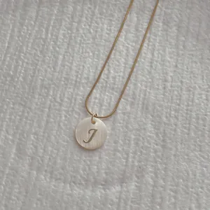 Detail of round shell pendant with golden letter J and fine snake chain necklace