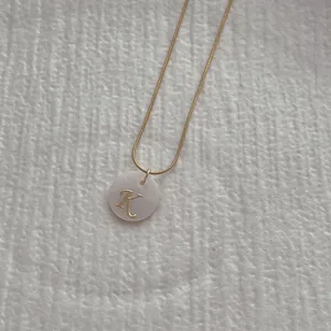 Close-up of golden letter K pendant with iridescent shell inlay on snake chain