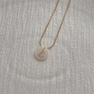 Detailed shot of golden snake chain necklace with natural shell letter L pendant