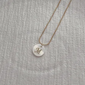 Macro shot of M-letter natural shell pendant with gold snake bone necklace detail
