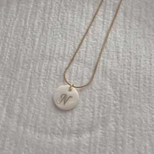 Macro detail of golden snake chain necklace featuring a white shell letter N pendant
