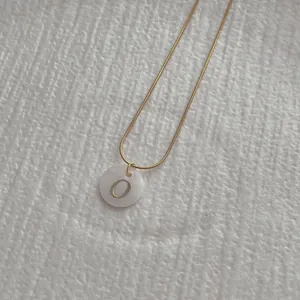 Macro shot of gold snake chain necklace with a white shell pendant featuring the letter O