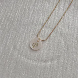 Macro shot of gold snake chain with white shell pendant featuring an engraved letter P