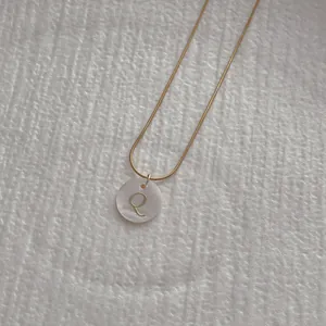 Close-up of golden snake chain with a white shell pendant featuring the letter Q