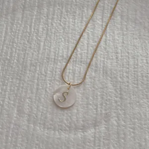 Detailed macro view of a gold snake chain necklace with an S-letter shell pendant