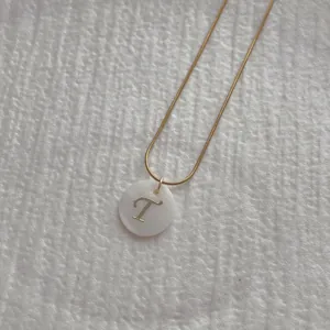 Close-up of golden snake chain and letter T engraved on white shell pendant necklace