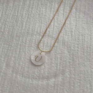 Macro detail of golden snake chain with shell pendant showing letter U engraving