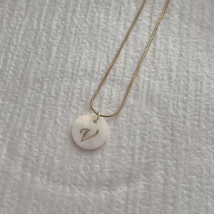 Detail shot of golden snake chain necklace with shell pendant featuring letter V