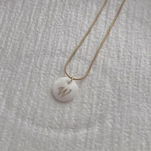 Close-up of golden snake chain with white shell letter W pendant on white texture