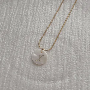 Detailed macro view of letter X shell pendant on a gold snake chain necklace
